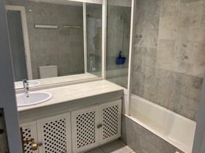 A bathroom with a white sink, a mirror, a bathtub, and a shower enclosure.