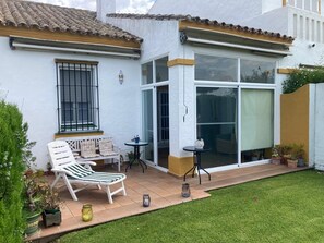 Una casa con patio, fachada blanca, techo de tejas y puerta corrediza de vidrio.