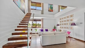 Ein modernes Interieur mit einer Holztreppe, einer weißen Sofagarnitur und einer Wand mit gerahmten Kunstwerken.