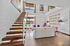 Un interior moderno con una escalera de madera, un conjunto de sofá blanco y una pared decorada con cuadros.