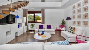 Ein modernes Wohnzimmer mit Treppe, weißen Sofas, einem Couchtisch und Kunstwerken an den Wänden.
