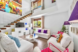 Una sala de estar moderna con una escalera, sofás blancos, una mesa de centro y un televisor.