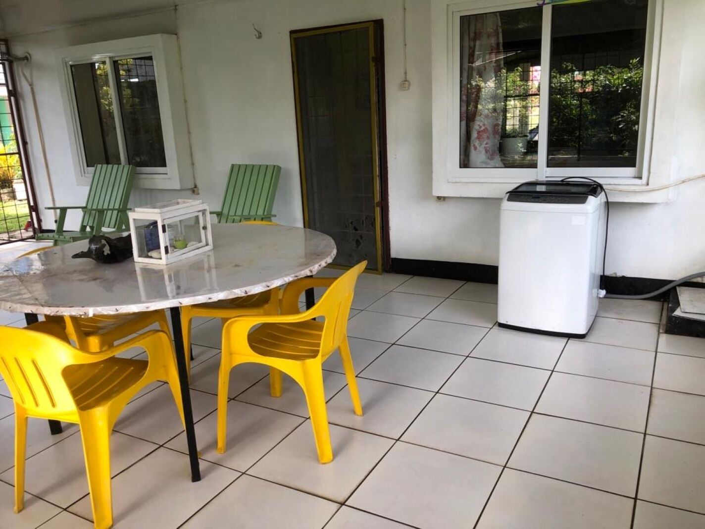 Een kamer met een ronde tafel, gele stoelen, een witte wasmachine en een raam met gordijn.