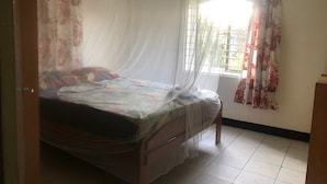 A single bed with a mosquito net, a window with a grid pattern, and a curtain with a floral design.