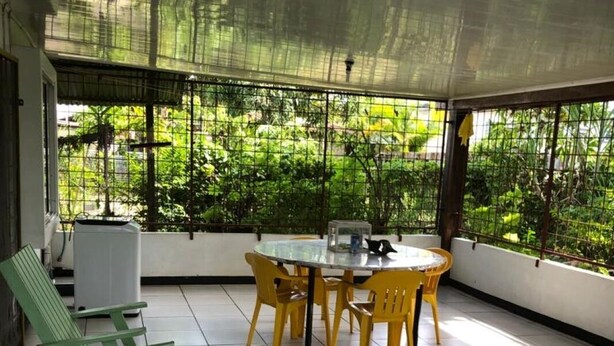 A covered patio area with a round table and chairs, a green bench, and a view of greenery through a mesh window.