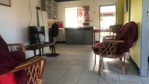 A living room with a television, a fan, and a dining area with chairs.