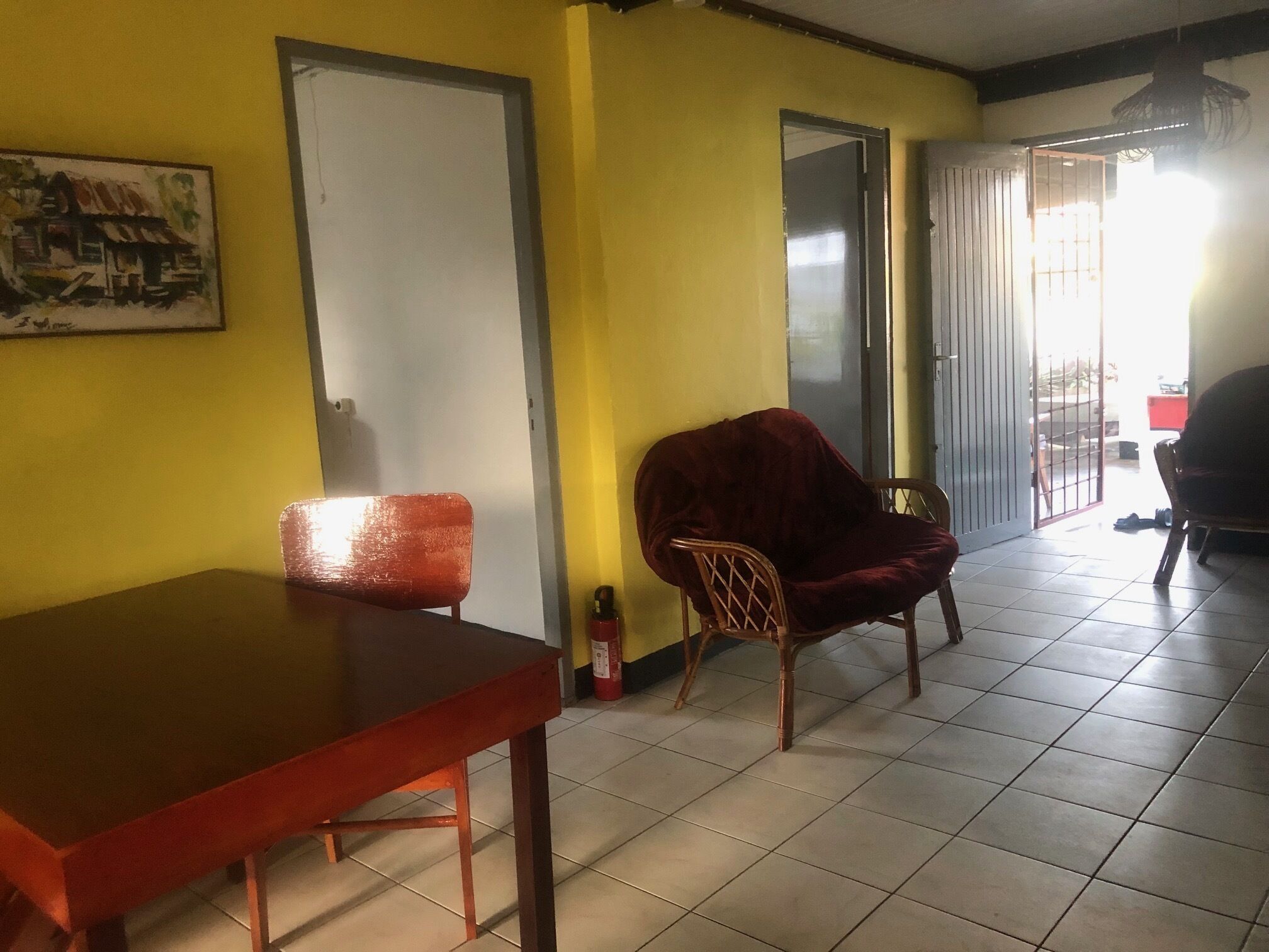 A room with a wooden table, a red chair, a door, and a yellow wall.