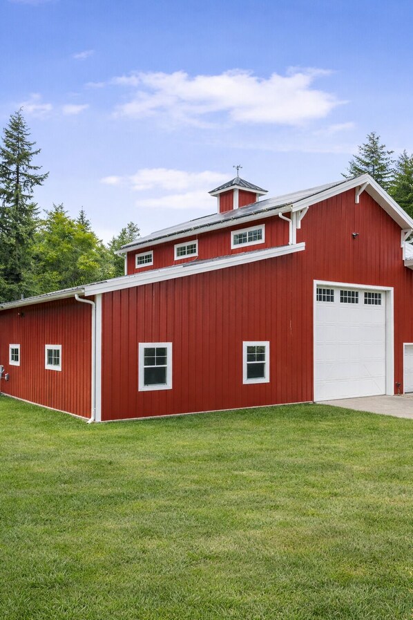 Une grange rouge avec une porte de garage blanche, entourée d’herbe verte et d’arbres.