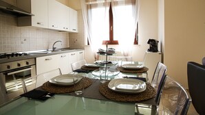 A modern kitchen with white cabinets, a glass dining table, and a window with curtains. - Bellavista Holiday Home (Abruzzo)