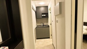 A narrow hallway leading to a kitchen with a microwave, cabinets, and a sink.