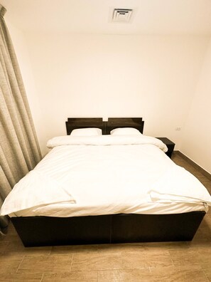 A single bed with a wooden frame, white bedding, and a nightstand with a lamp.