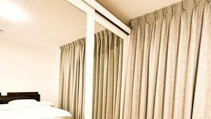 A hotel room with a bed, a large mirror, and beige curtains. - Central Apartment For Rent 30 (Amman)
