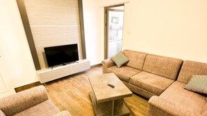 A modern living room with a sectional sofa, a coffee table, and a flat-screen TV mounted on a wall.