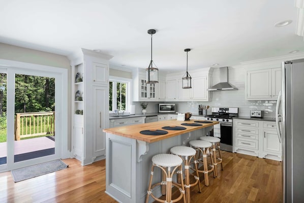 A spacious kitchen with white cabinetry, a central island with stools, a large window, and a deck area.