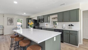 A modern kitchen with a large island, bar stools, and a view of the outside. - Spacious & Cozy ~ Close to Fort Moore ~ Pool Table (Columbus)