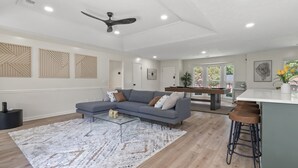 A modern living room with a grey sofa, a glass coffee table, and a ceiling fan. - Spacious & Cozy ~ Close to Fort Moore ~ Pool Table (Columbus)