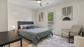 A bedroom with a bed, a chair, a desk, and a window with a view of the outside.