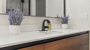 A modern bathroom with a white sink, black faucet, and two potted lavender plants. - Spacious & Cozy ~ Close to Fort Moore ~ Pool Table (Columbus)