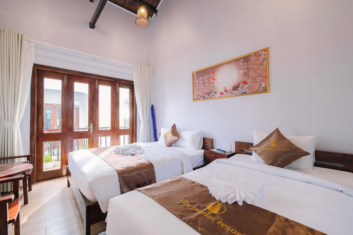 A hotel room with two beds, a wooden desk, and a large window with curtains.