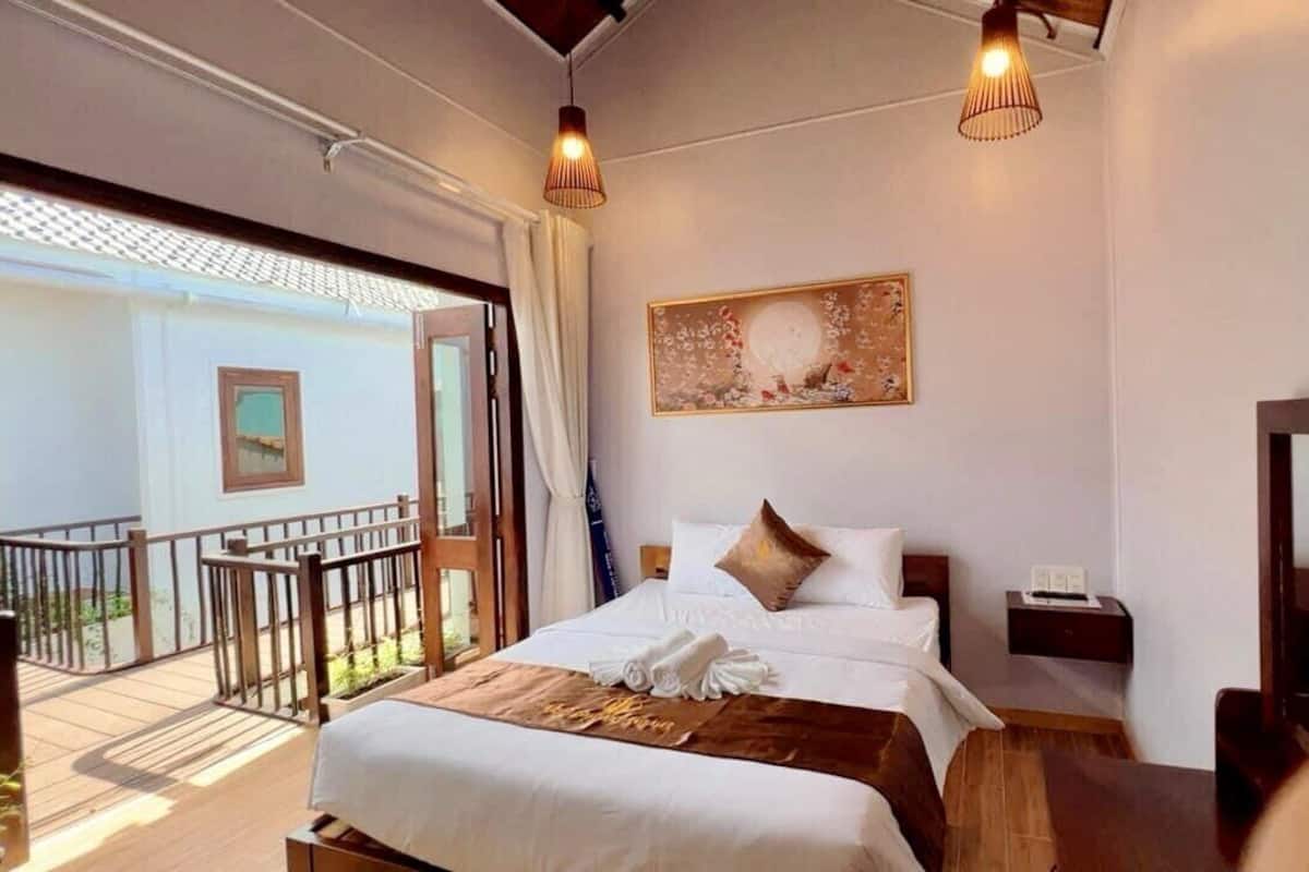 A hotel room with a large bed, a balcony, a painting on the wall, and a wooden floor.