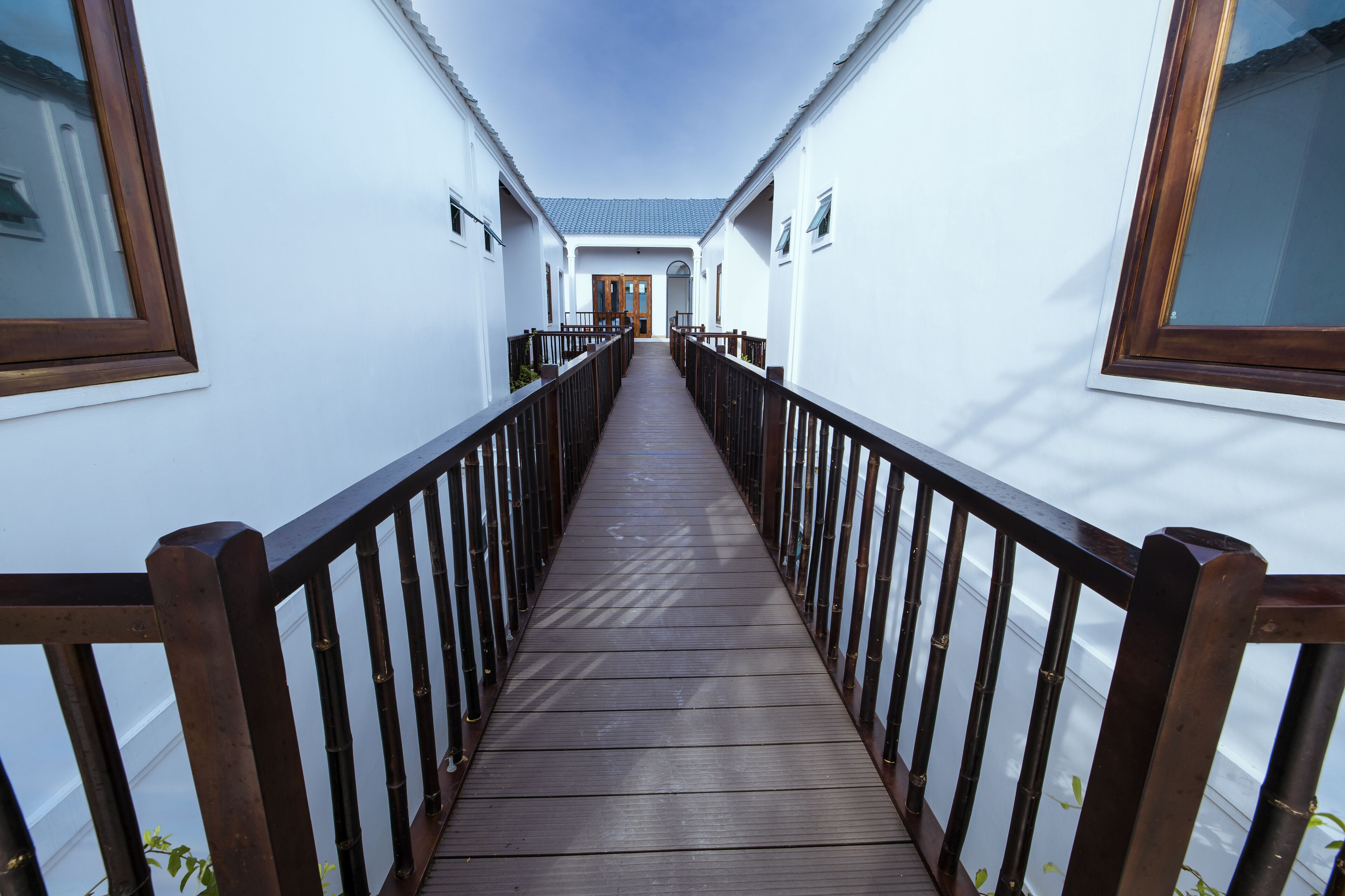 A corridor with wooden railings, white walls, and a wooden floor leading to a door at the end.