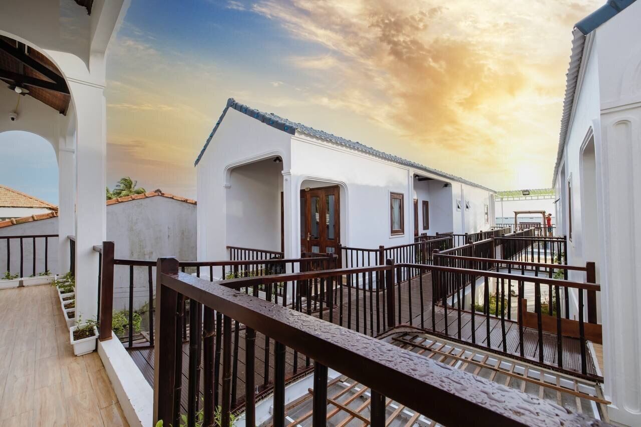 Une cour bordée de bâtiments blancs, un escalier en bois et une vue sur la mer.