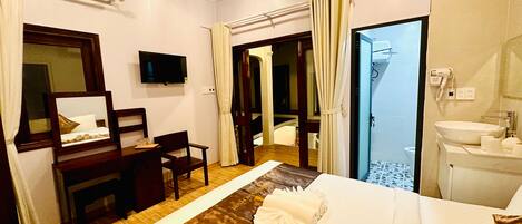 A hotel room with a bed, a desk, a television, a bathroom with a sink and mirror, and curtains.