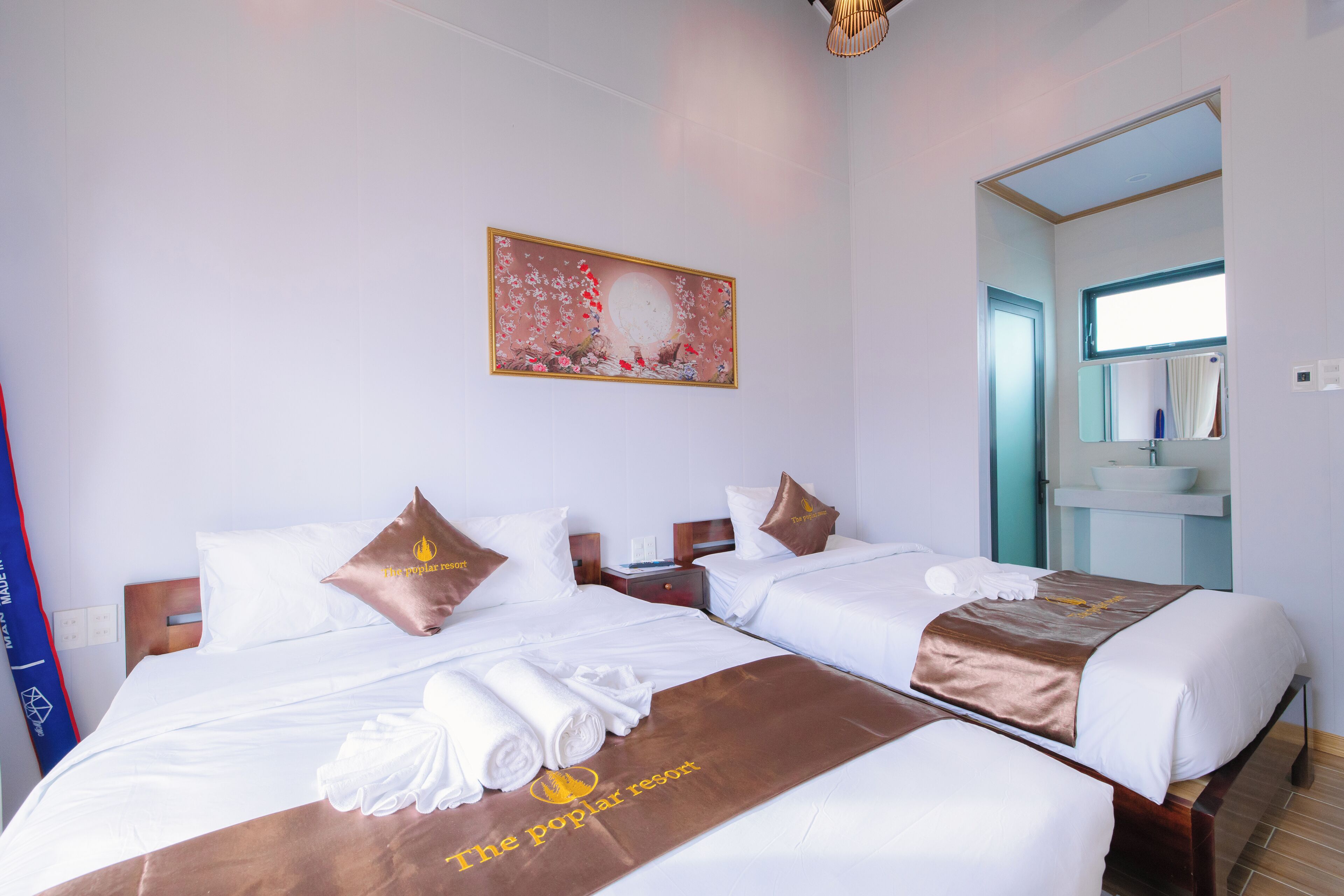 Habitación de hotel con dos camas, un cuadro en la pared, baño con lavamanos y espejo, y toallas sobre las camas.