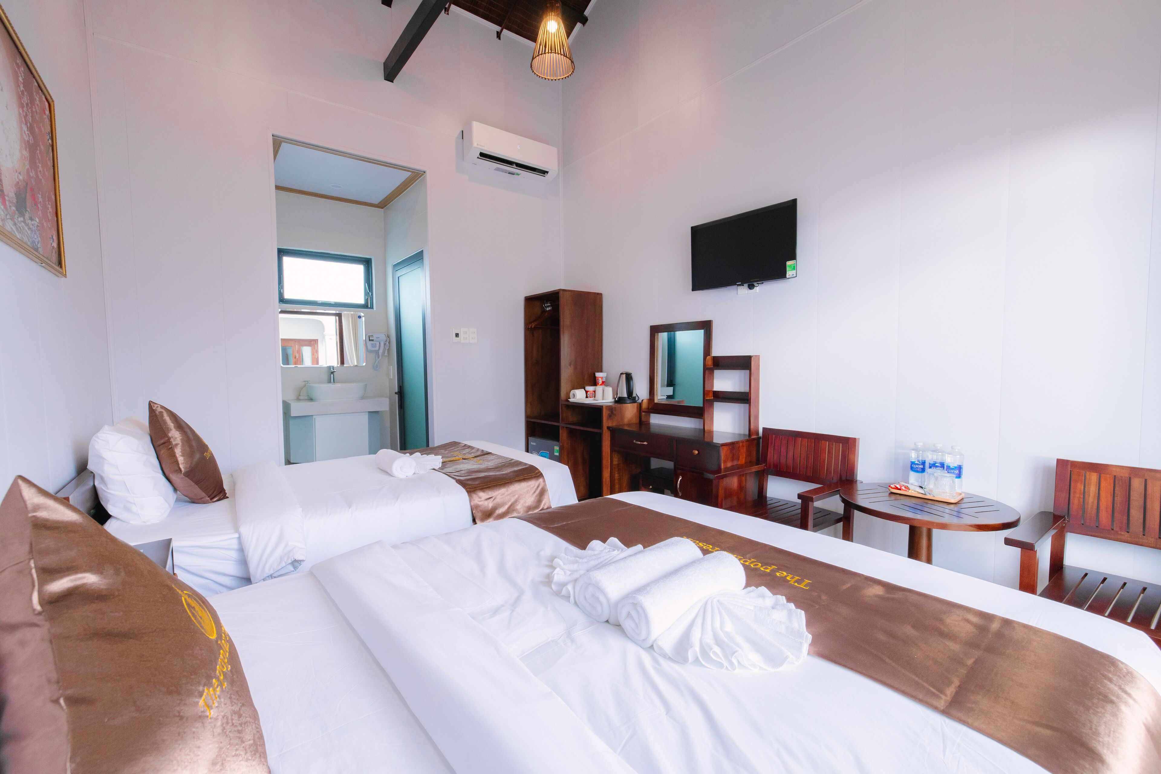 A hotel room with two beds, a desk, a chair, a TV, and an air conditioning unit.