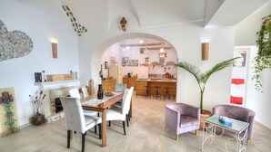 Amplia sala de estar con mesa de comedor, asientos cómodos, una cocina al fondo y una planta grande.