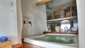 Una habitación con un banco de madera, una bañera blanca y un estante con botellas y una escalera.