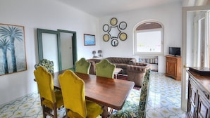 Un coin repas avec une table en bois et des chaises jaunes, un canapé marron et un téléviseur posé sur un meuble en bois.