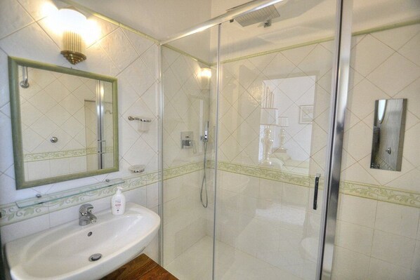 Un baño con ducha envuelta en vidrio, un lavabo con espejo y una lámpara sobre el espejo.