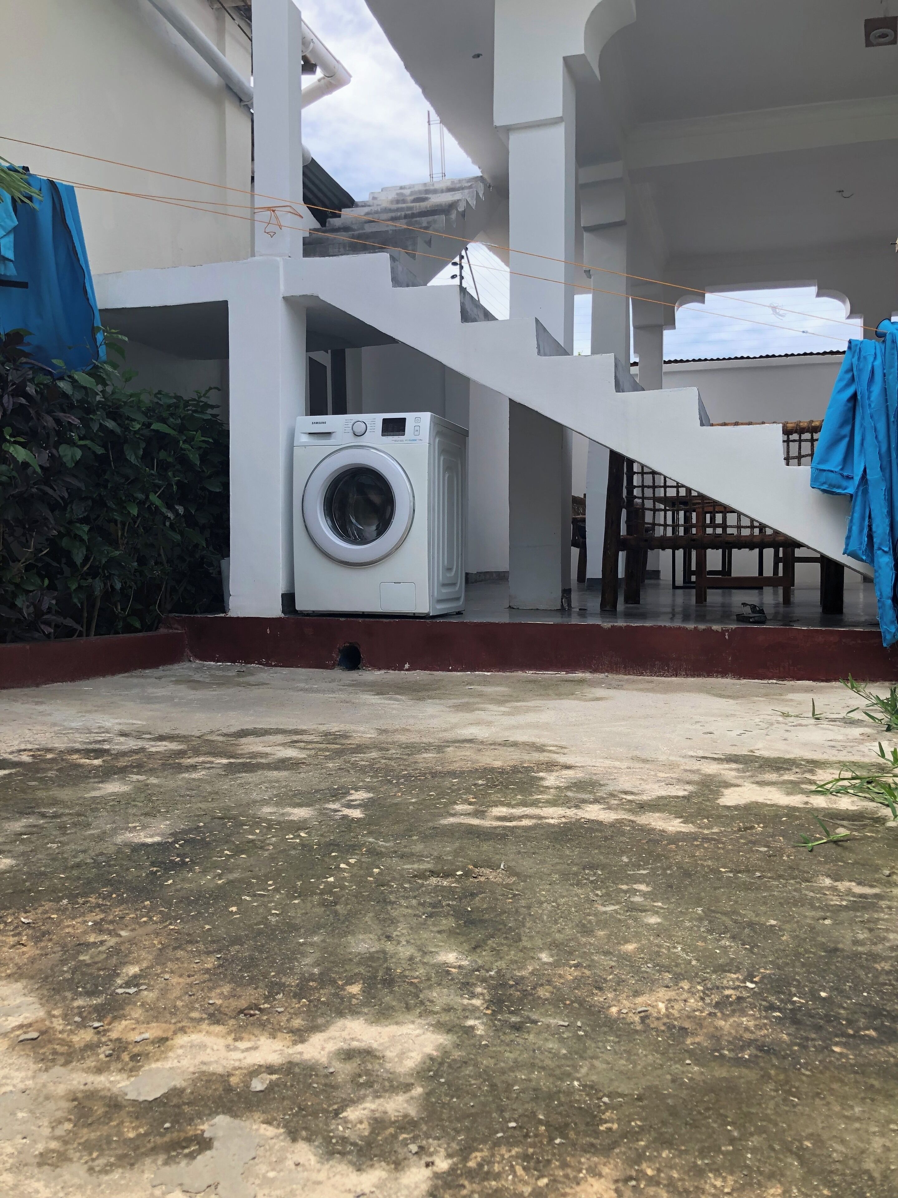 A laundry area with a washing machine, a staircase, and a covered outdoor seating area.