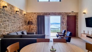 Un amplio espacio de estar con pared de piedra, un ventanal grande, un sofá, un televisor y una mesa de comedor con sillas.
