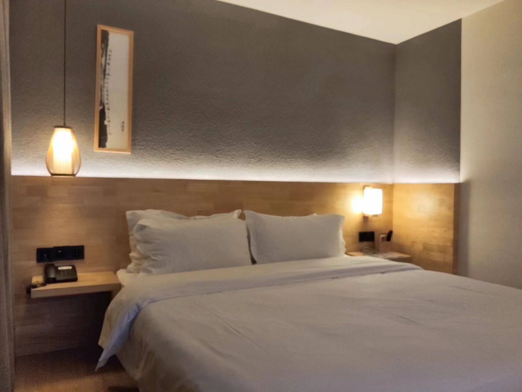 Une chambre d’hôtel avec un grand lit, deux tables de chevet et des lampes fixées au mur.