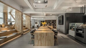 Une salle de conférence moderne, dotée d’une longue table en bois, de chaises noires et d’un vase central orné de fleurs jaunes.