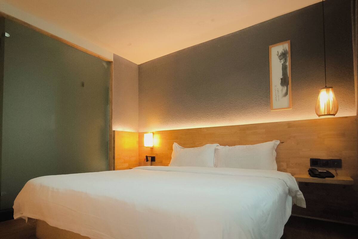 A hotel room with a large bed, a bedside table with a phone, and a wall-mounted light fixture.