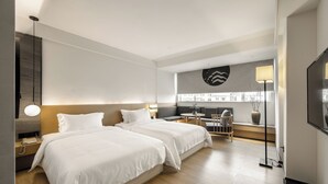 Une chambre d’hôtel moderne avec deux lits, un canapé, une petite table et un téléviseur.