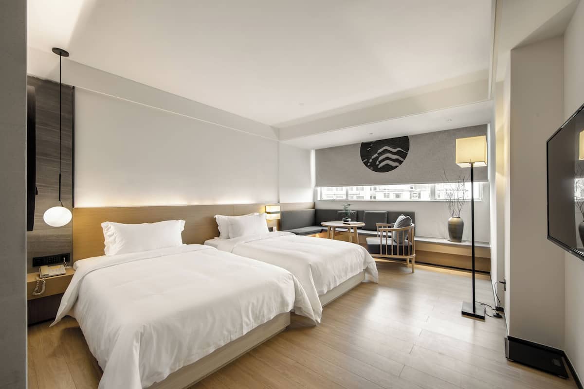 A modern hotel room with two beds, a sofa, a small table, and a TV.