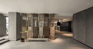 Um interior moderno com um divisório de madeira tradicional, um banco de pedra e uma área de recepção ao fundo.