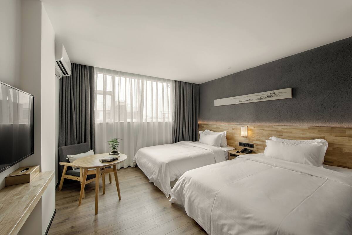A hotel room with two beds, a TV, a desk, and a window with curtains.