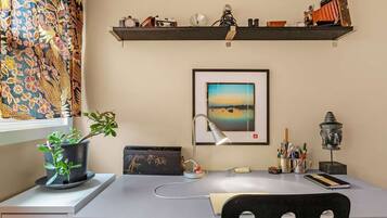 Ein Arbeitsplatz mit Schreibtisch, Stuhl, Topfpflanze, Lampe und einem gerahmten Bild an der Wand.