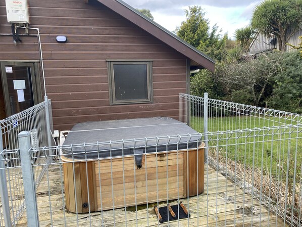 Une cabane en bois avec une clôture en métal, un jacuzzi et une petite terrasse.