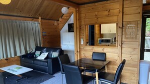 Ein gemütliches Cabin-Interieur mit Holzvertäfelung, einer schwarzen Ledersofa, einem Esstisch mit Stühlen und einer Küchenzeile mit einer Mikrowelle.