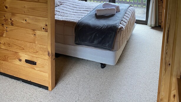 Ein gemütlicher Holzraum mit einem großen Bett, einer runden Leuchte und Blick auf Grünflächen.