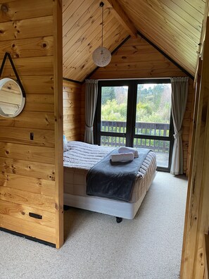 Une pièce chaleureuse aux murs en bois, avec un grand lit, un luminaire rond et une vue sur la verdure.