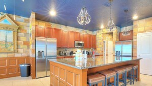 Una cocina con una isla central, electrodomésticos de acero inoxidable, armarios de madera y taburetes de bar.