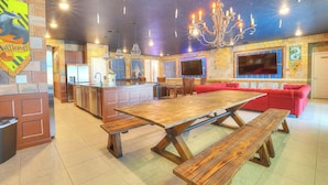 Una cocina amplia con una gran mesa de madera y bancos, un sofá rojo y un televisor montado en la pared.