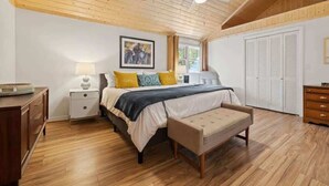 A bedroom with a wooden ceiling, a bed with yellow and blue pillows, a bedside table with a lamp, and a wardrobe. - Bright 2BR House w/ Sunroom + Fire Pit~Near Trails~Free Tickets (Hendersonville)
